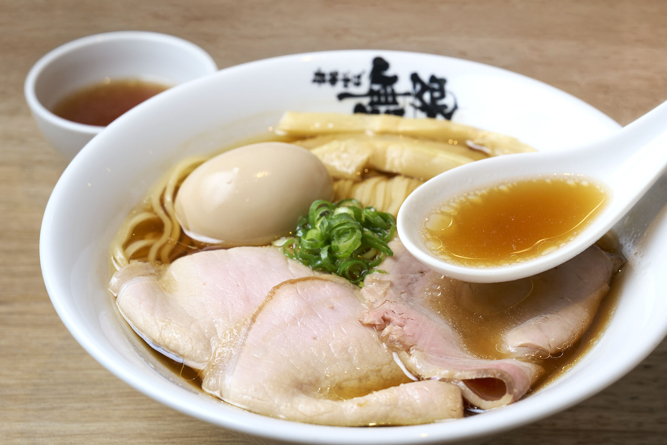 特選中華そばのスープをレンゲにすくった様子。奥には小さな器があり、少量取り分けたスープが入っている。