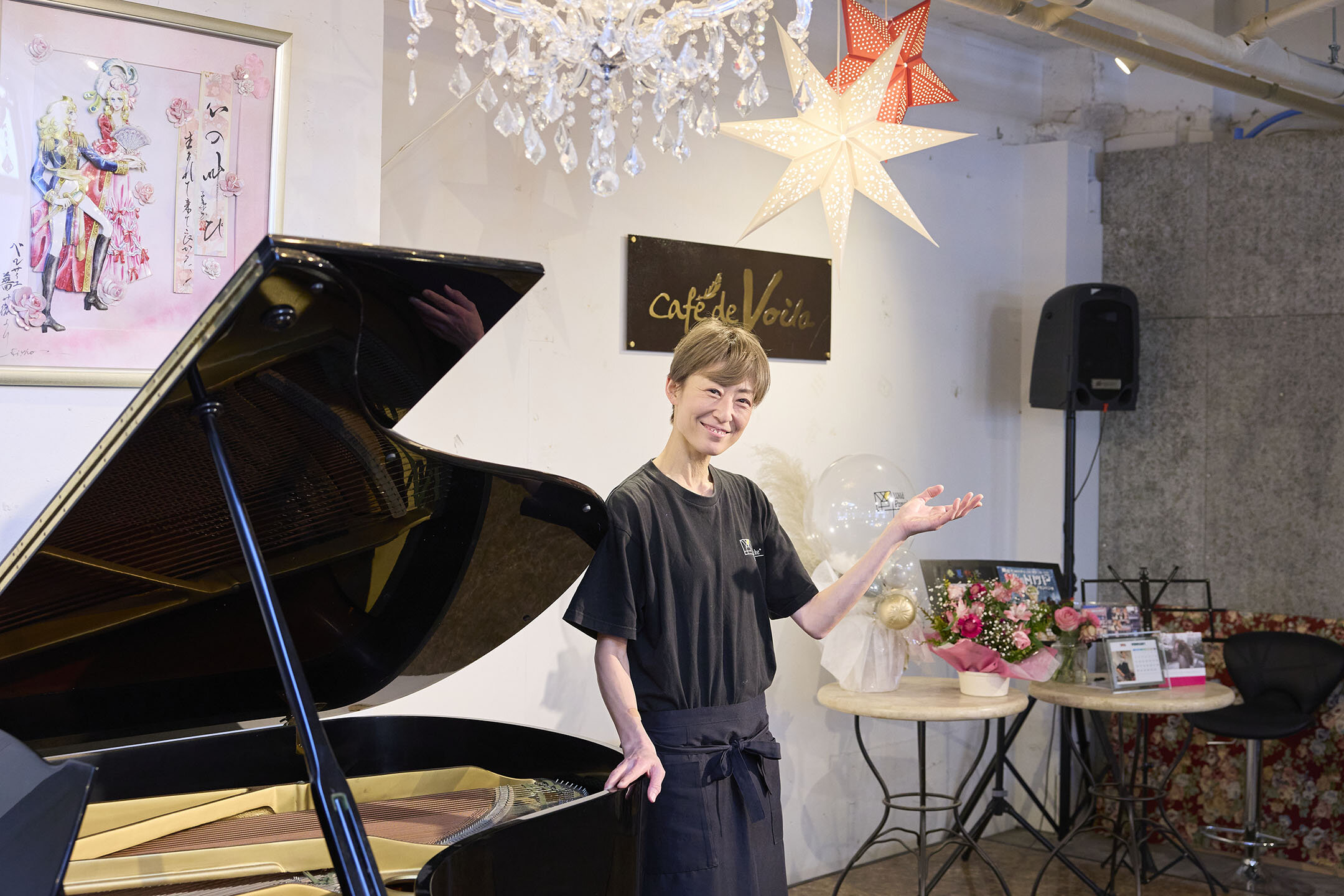 グランドピアノの前に立ち、「ようこそ」のポーズをとるマネージャーの汐美真帆さん。