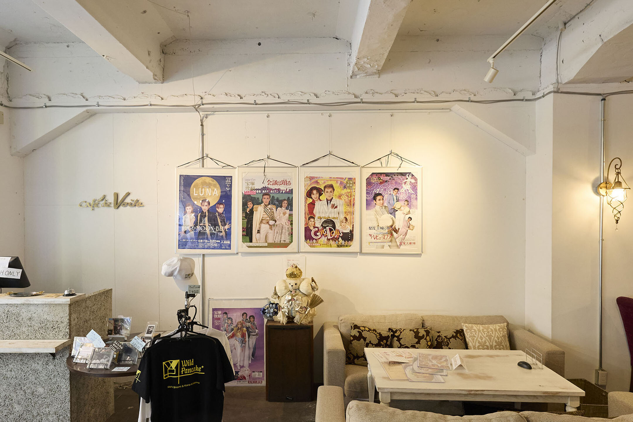 宝塚歌劇団のポスターが4枚、壁にかけられている。TシャツやCDなどのグッズも販売されている様子。