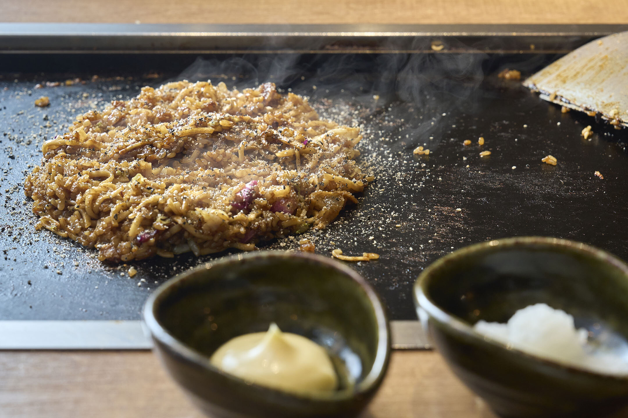 鉄板にできたての「そばめし」。手前にはマヨネーズと大根おろしが入った小さな器が並ぶ。