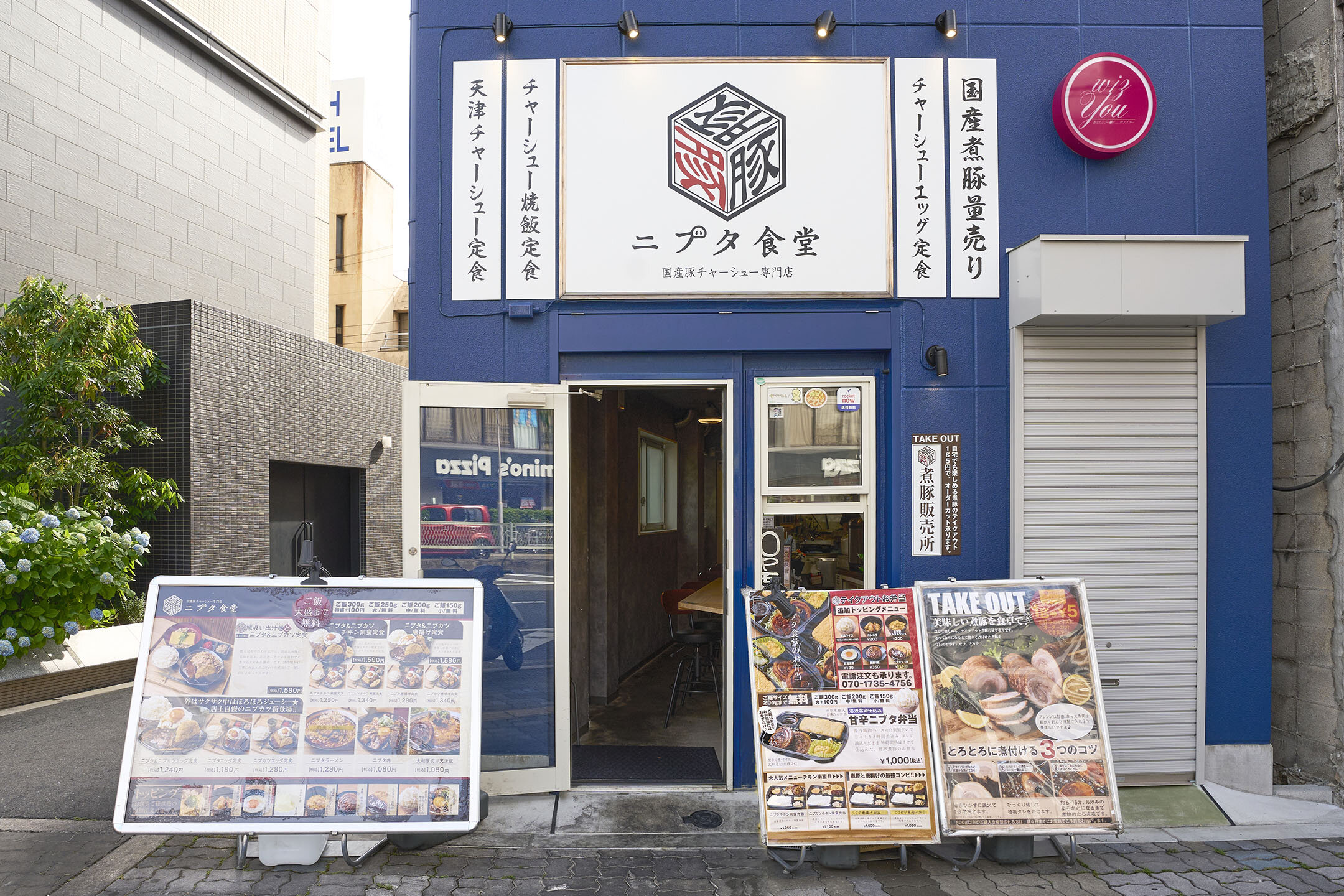 青い壁が印象的なニブタ食堂の外観。メニューの看板が店の前に置かれている。