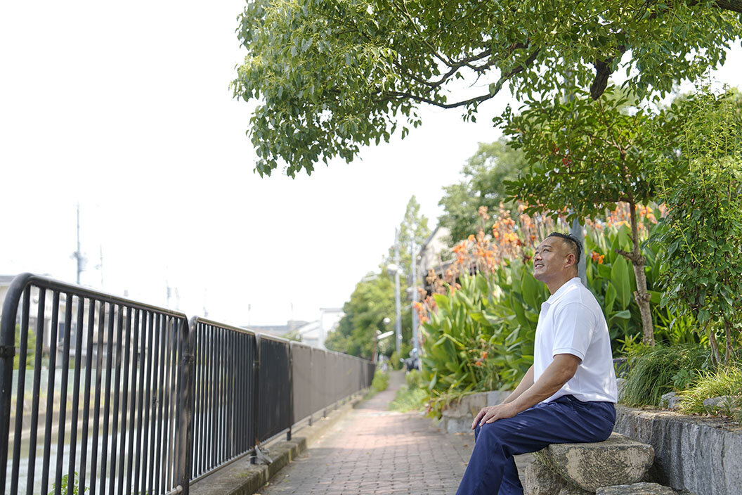 疏水沿いの遊歩道のベンチで休憩する長谷川さん