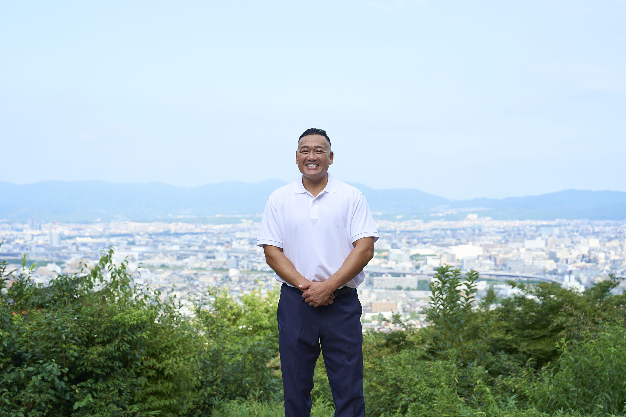 京都市街の景色を背に、稲荷山の「四ツ辻」に立つ長谷川さん