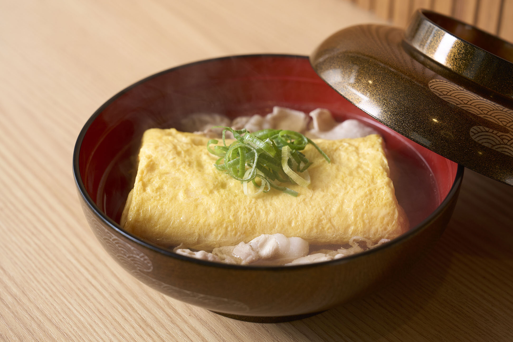 大きなお椀に入ったお店名物「豚吸いの出汁巻」。中が見えるようにフタがずらしてある。