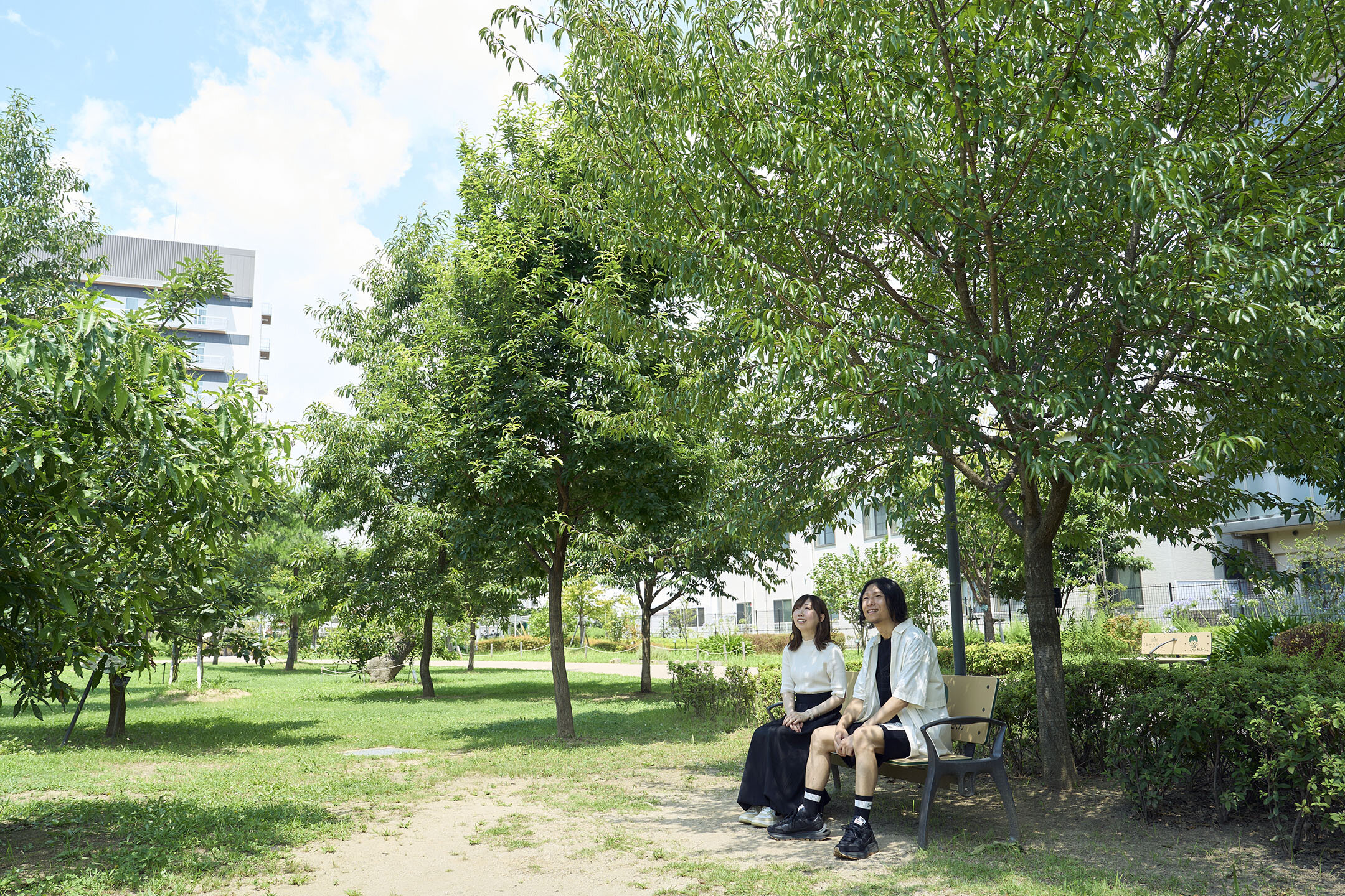 『キセラ川西せせらぎ公園』の、木陰のベンチに腰掛けるイケダさん夫妻