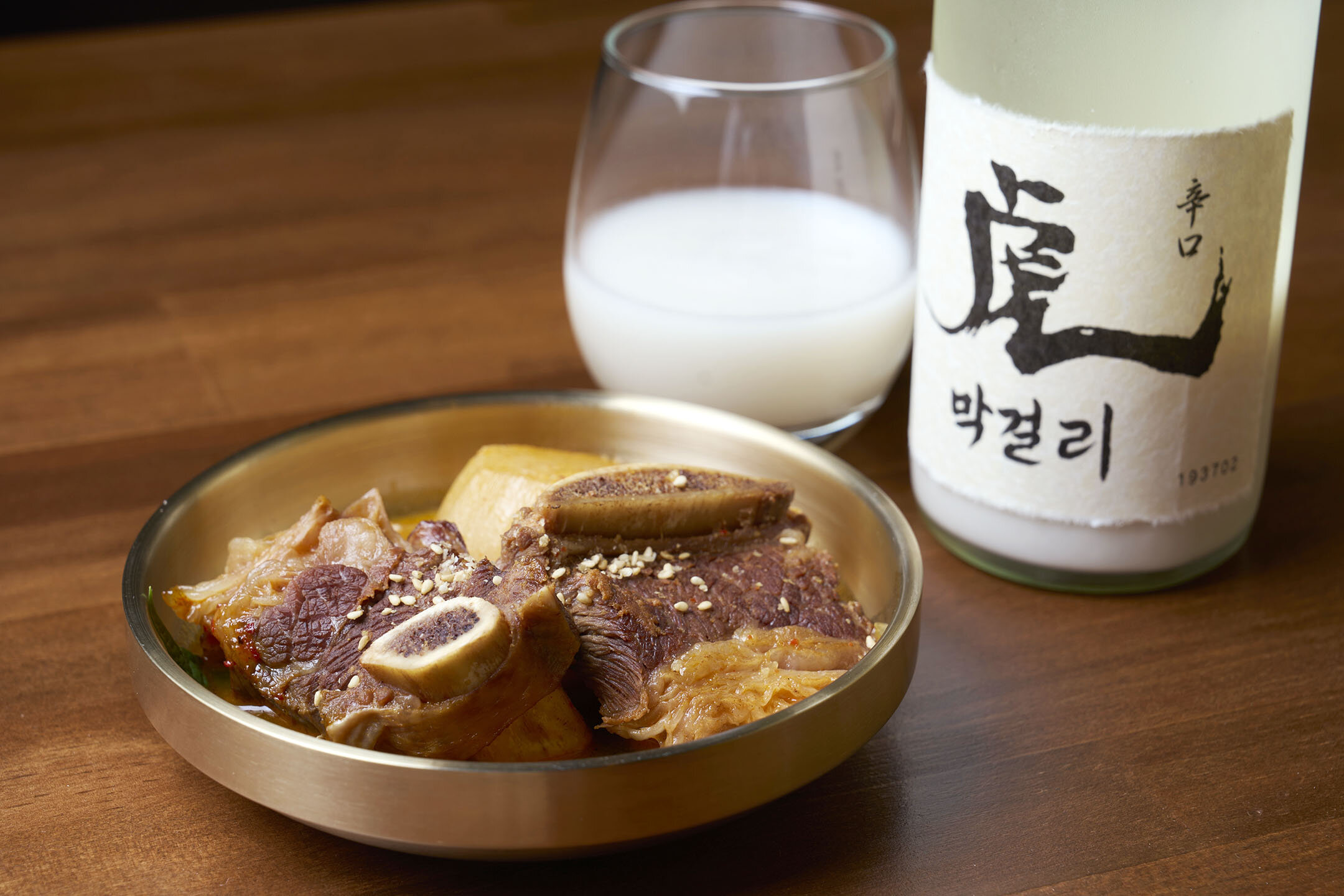 骨付きカルビチムと、右上にはグラスに注がれた「虎 辛口生まっこり」とボトル。