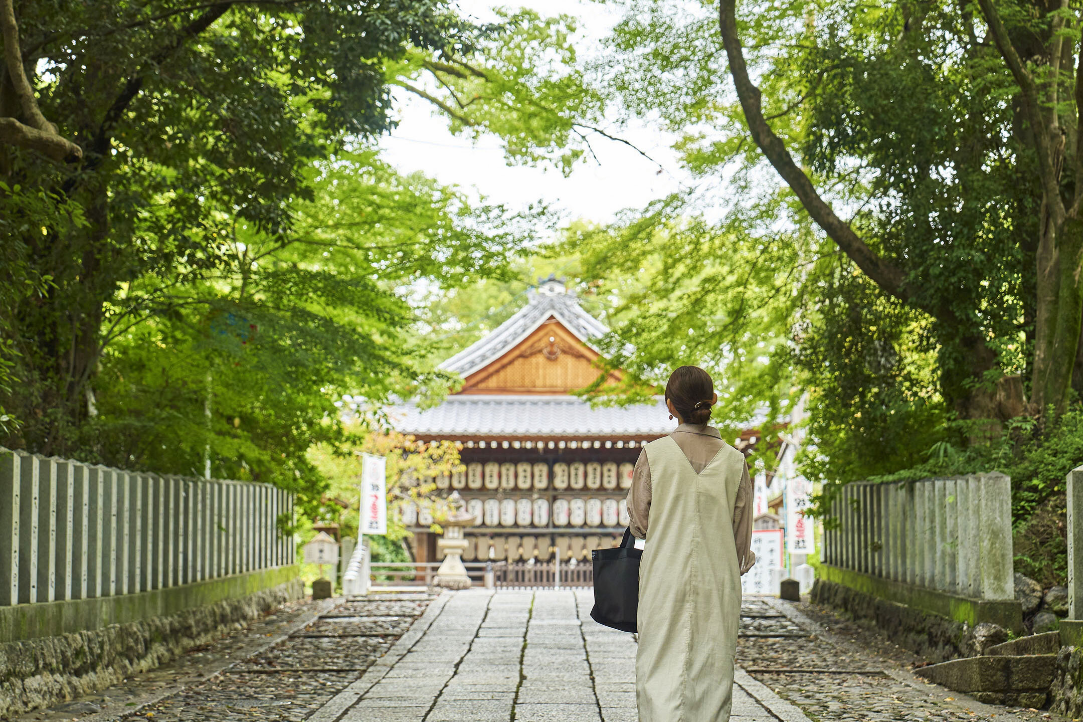 緑いっぱいの参道を抜けて本殿に向かう由紀子さんの後ろ姿