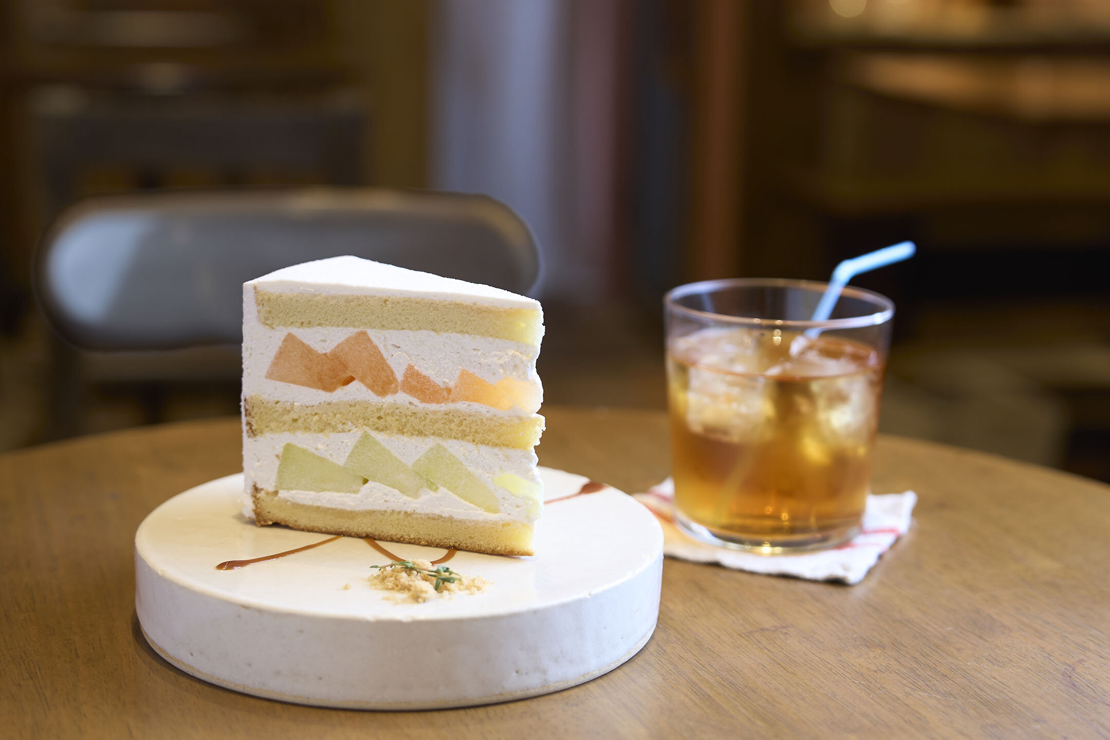 オレンジ色と薄い緑色、2種類のメロンがたっぷり入ったショートケーキ。ケーキの右横には、アイスティーが添えられている。
