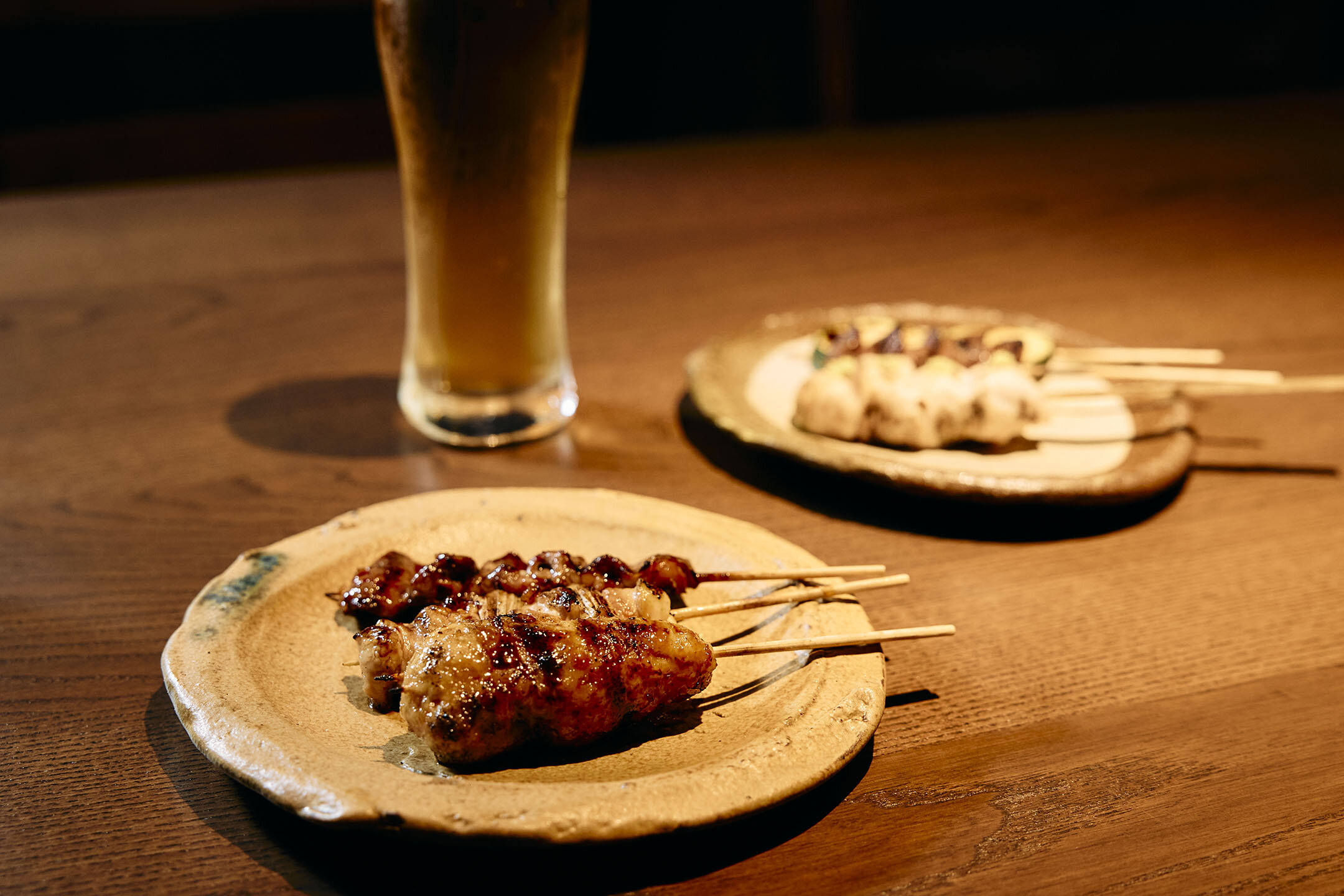 塩つくね串、ねぎま串、ハツ串がのった皿の奥には生ビール