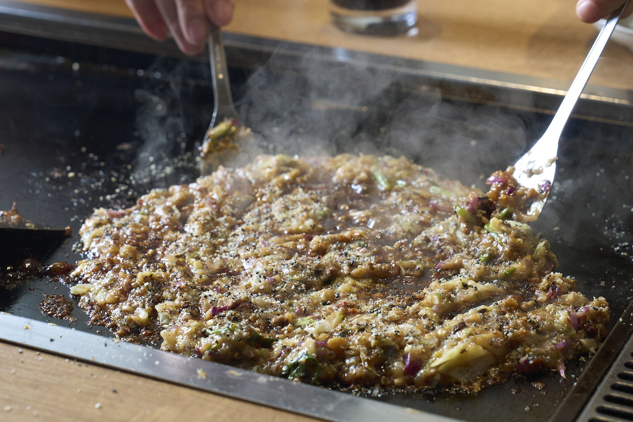 「発酵羊肉もんじゃ」を小さなへらで混ぜているところ。湯気がたっている。