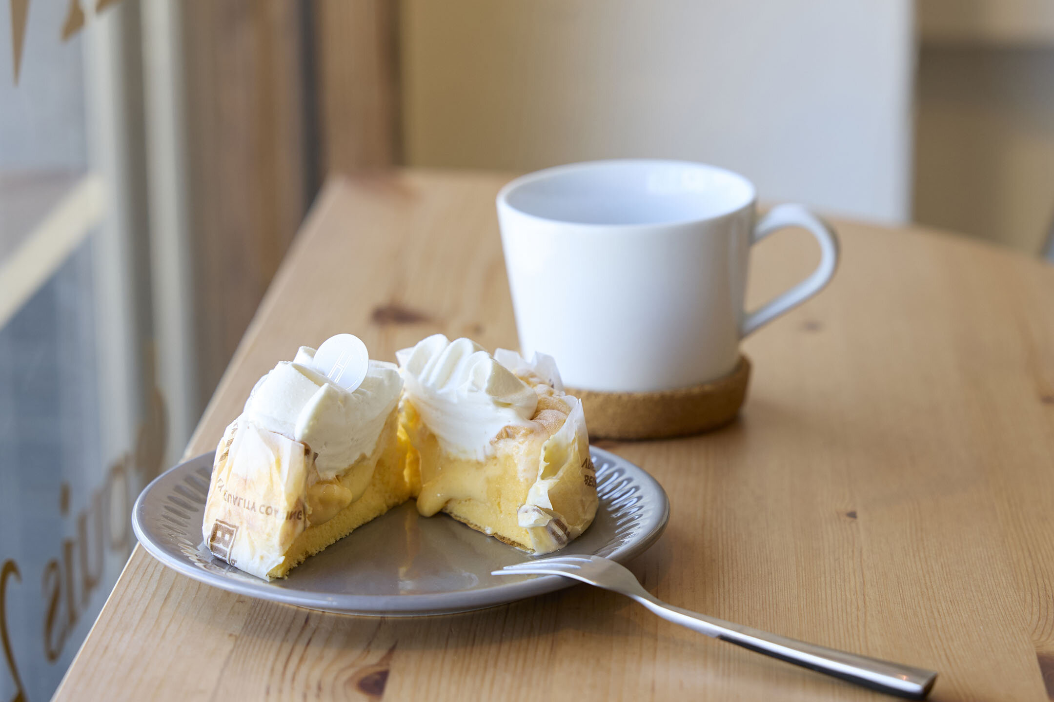 人気のケーキ「パンデロー」を半分にカットし、とろりとクリームが出てくる様子。奥にはマグカップが