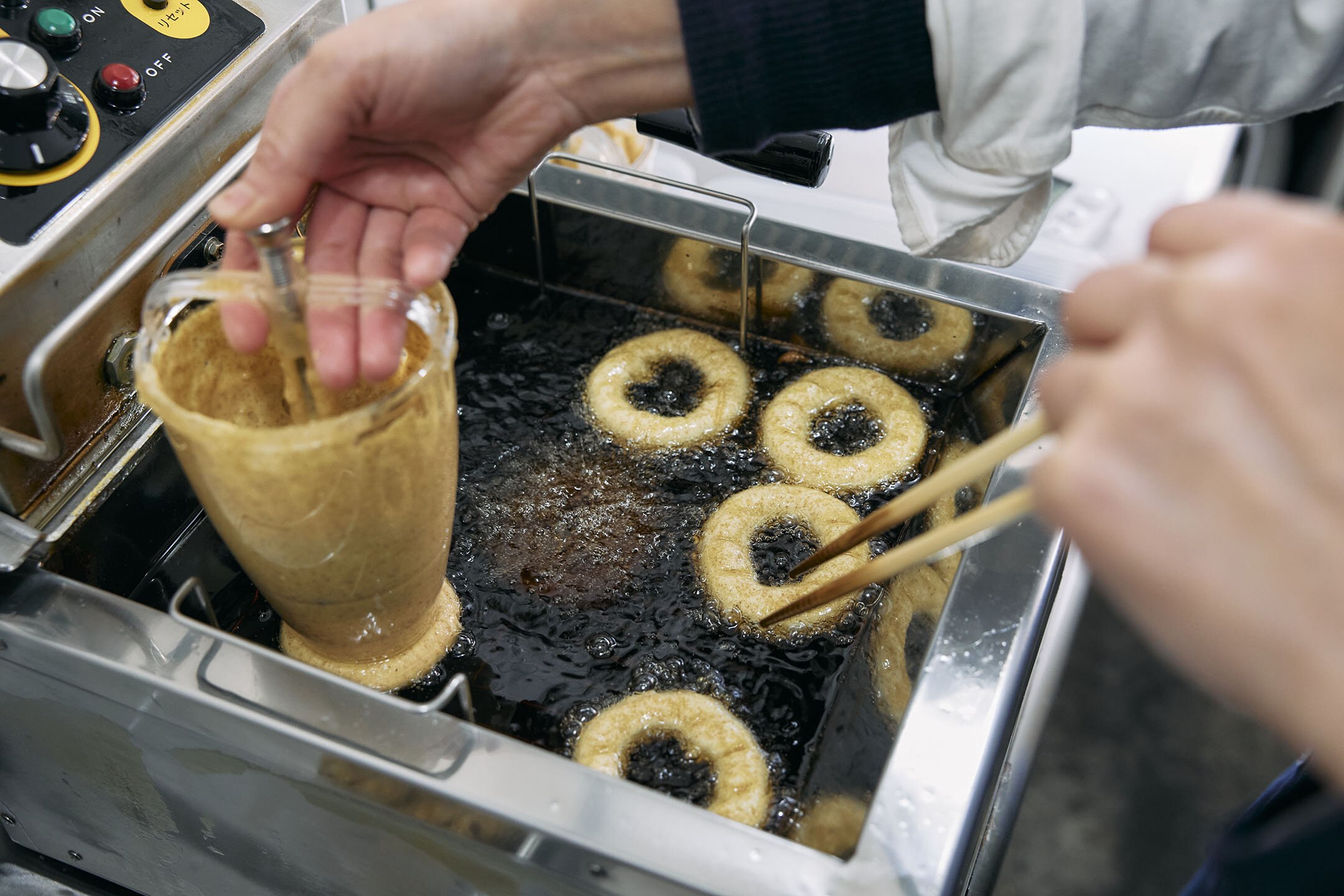 店主がドーナツメーカーで豆乳ドーナツを揚げている様子