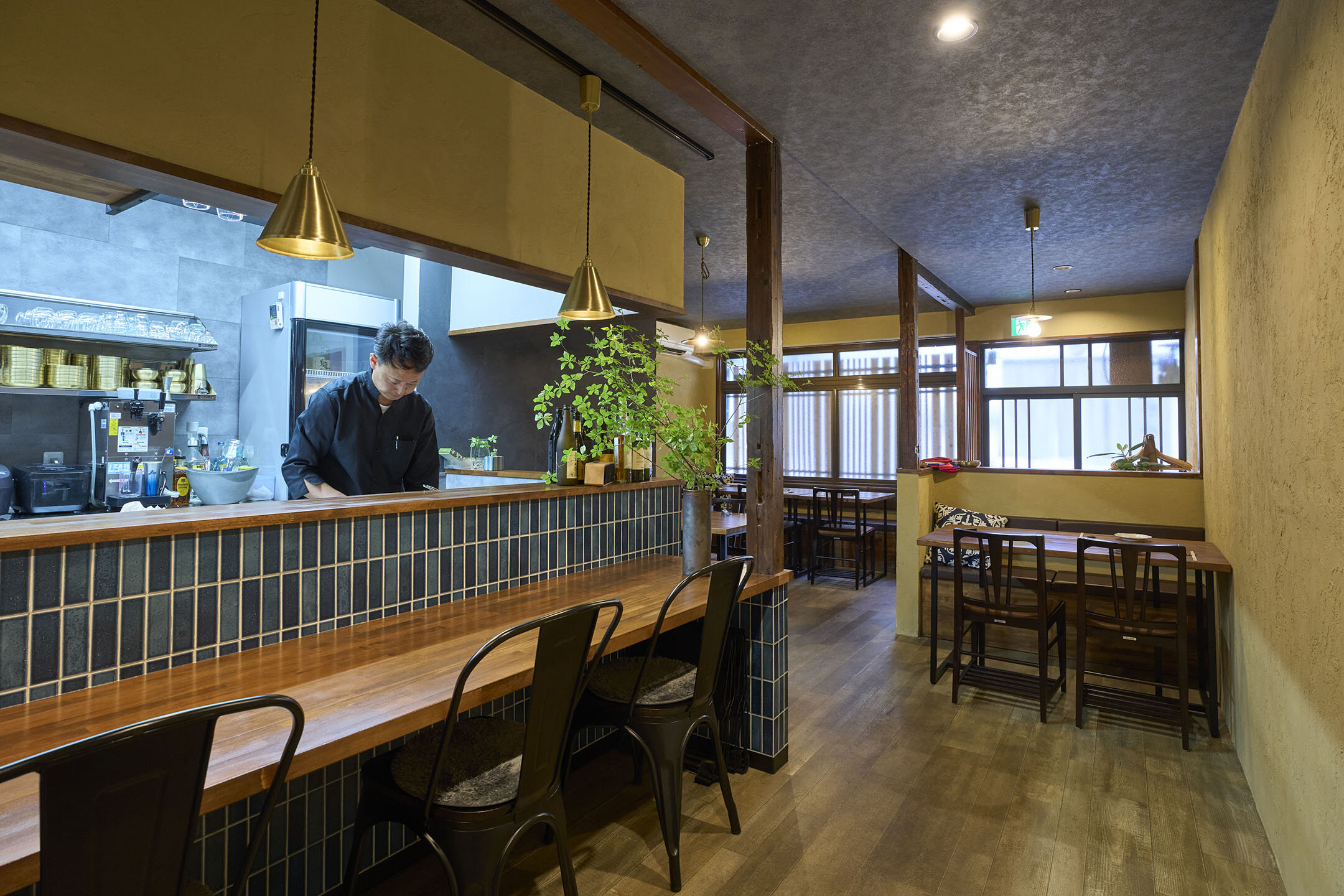 カウンター席とテーブル席のある店内。オーナーシェフがカウンター内で調理している様子。