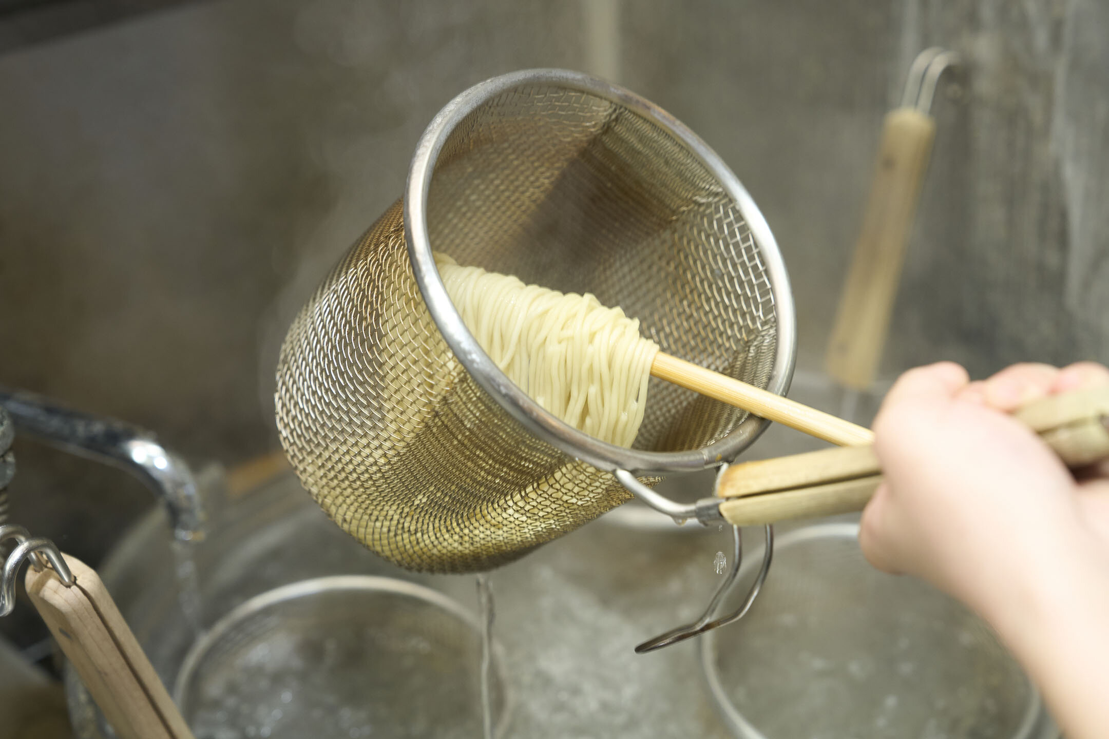 深さのあるザルにゆでたての麺が入っていて湯切りをしている様子。